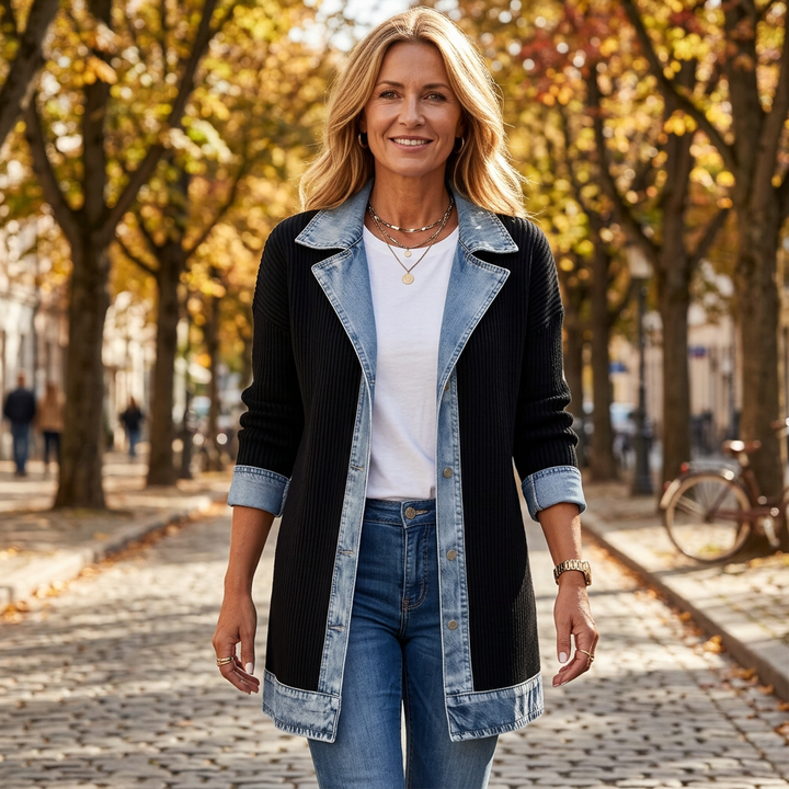 Femme souriante marchant sur une rue pavée bordée d'arbres d'automne, manteau noir côtelé à bords en denim, t-shirt blanc et jean. 1