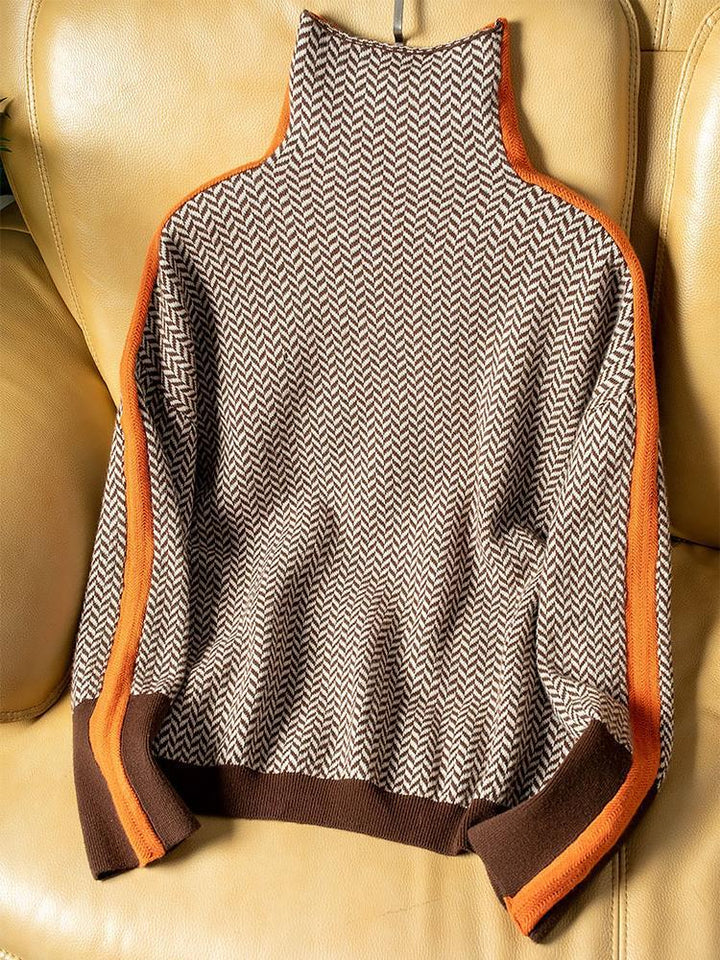 Pull à chevrons marron et beige posé à plat sur un fauteuil en cuir, liserés orange sur les épaules et manches. 5