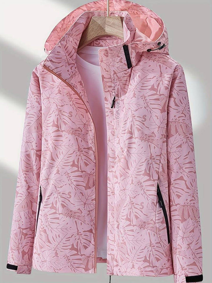 Veste rose à imprimé de grandes feuilles, capuche à cordon, zip ouvert laissant voir un t-shirt clair, sur cintre en bois. 4