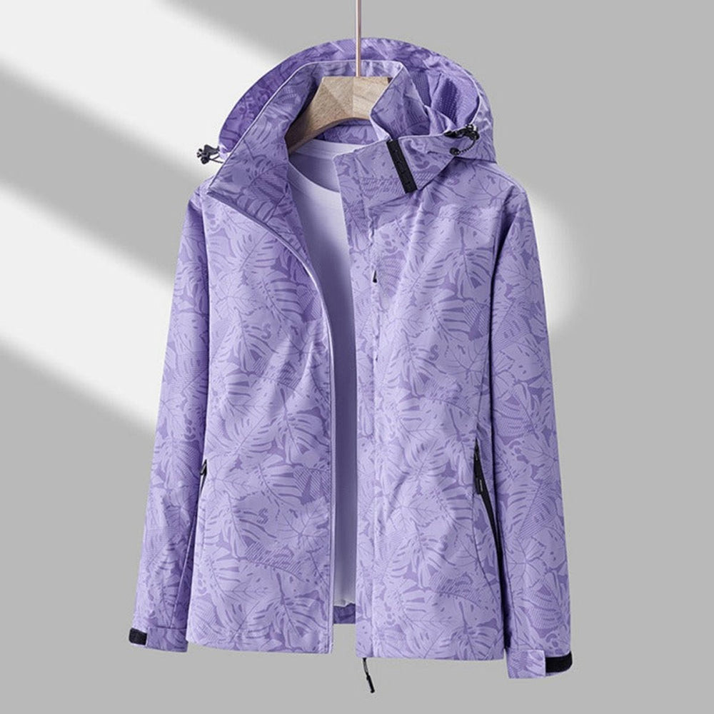 Même veste lilas à feuilles tropicales vue de face sur cintre, avec cordons de capuche, poches zippées et poignets à bandes noires. 2