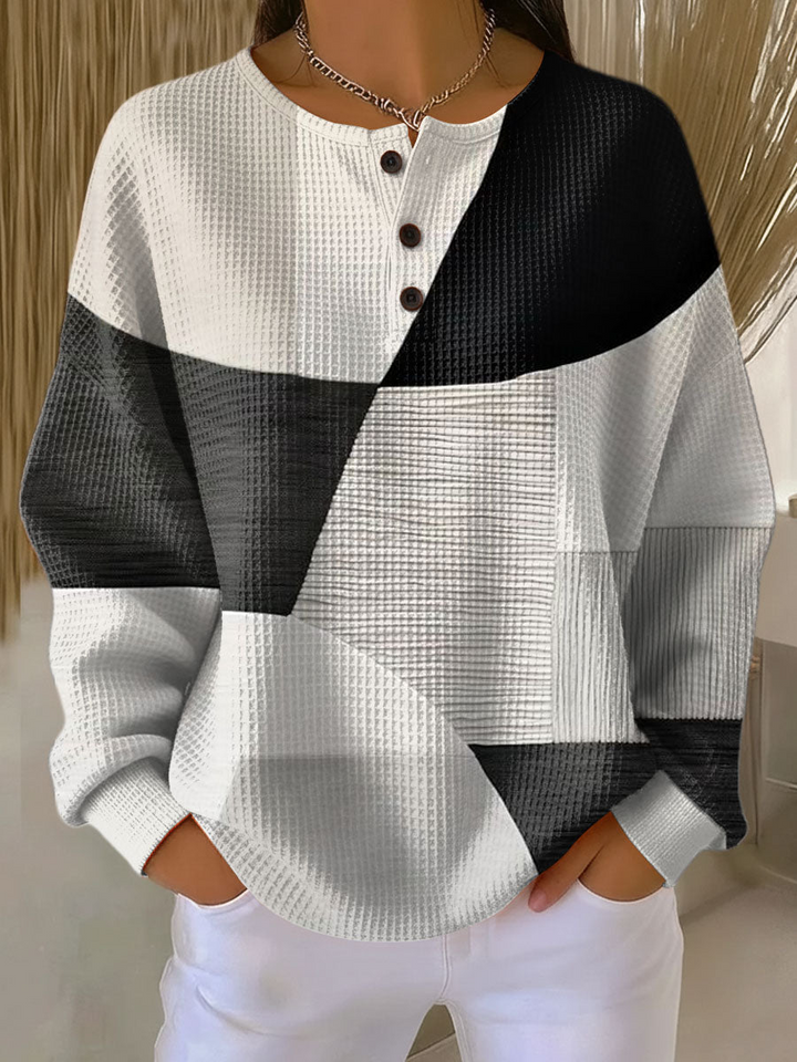 Pull gaufré à col tunisien et trois boutons, patchwork géométrique noir, gris et blanc, porté avec un pantalon blanc. 2