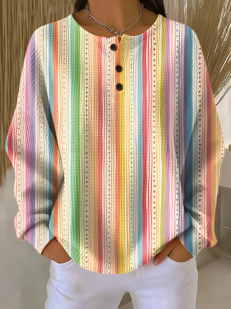 Pull gaufré à rayures verticales arc-en-ciel et petits pointillés, col à trois boutons, porté avec un pantalon blanc. 10