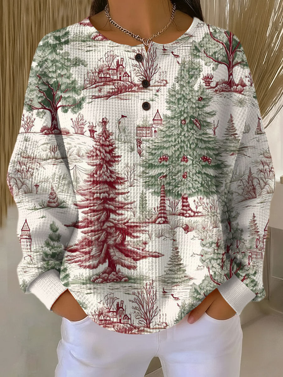 Pull gaufré blanc cassé à col boutonné, porté par une mannequin, motif de sapins verts et rouges et de maisons en campagne. 22