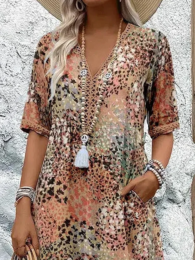 Gros plan sur le buste de la robe beige et orangé: col V bordé de dentelle, manches courtes, longs colliers de perles. 6