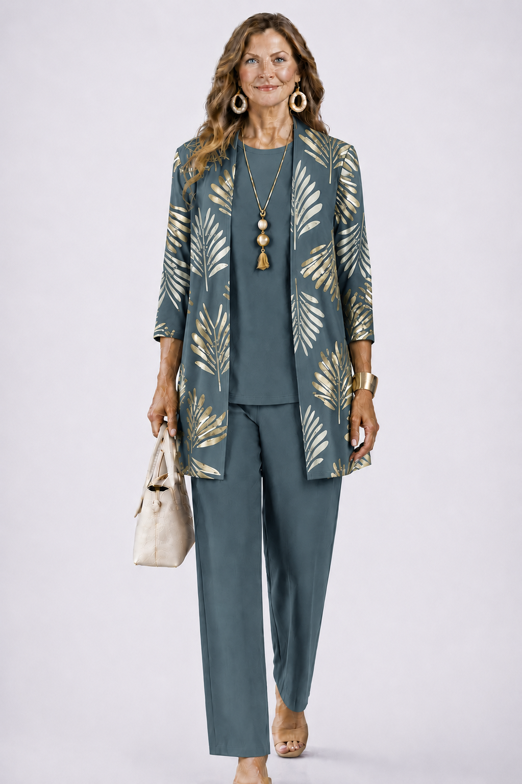 Femme en ensemble bleu-gris avec cardigan ouvert à grandes feuilles dorées, haut uni et pantalon droit, sac beige à la main. 1