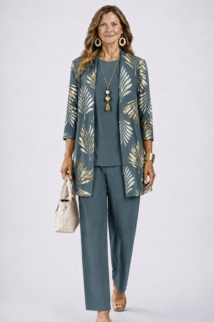 Femme en ensemble bleu-gris avec cardigan ouvert à grandes feuilles dorées, haut uni et pantalon droit, sac beige à la main. 1