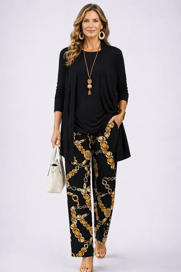 Femme en cardigan et haut noirs unis, pantalon noir imprimé de chaînes dorées, sac clair à la main. 17