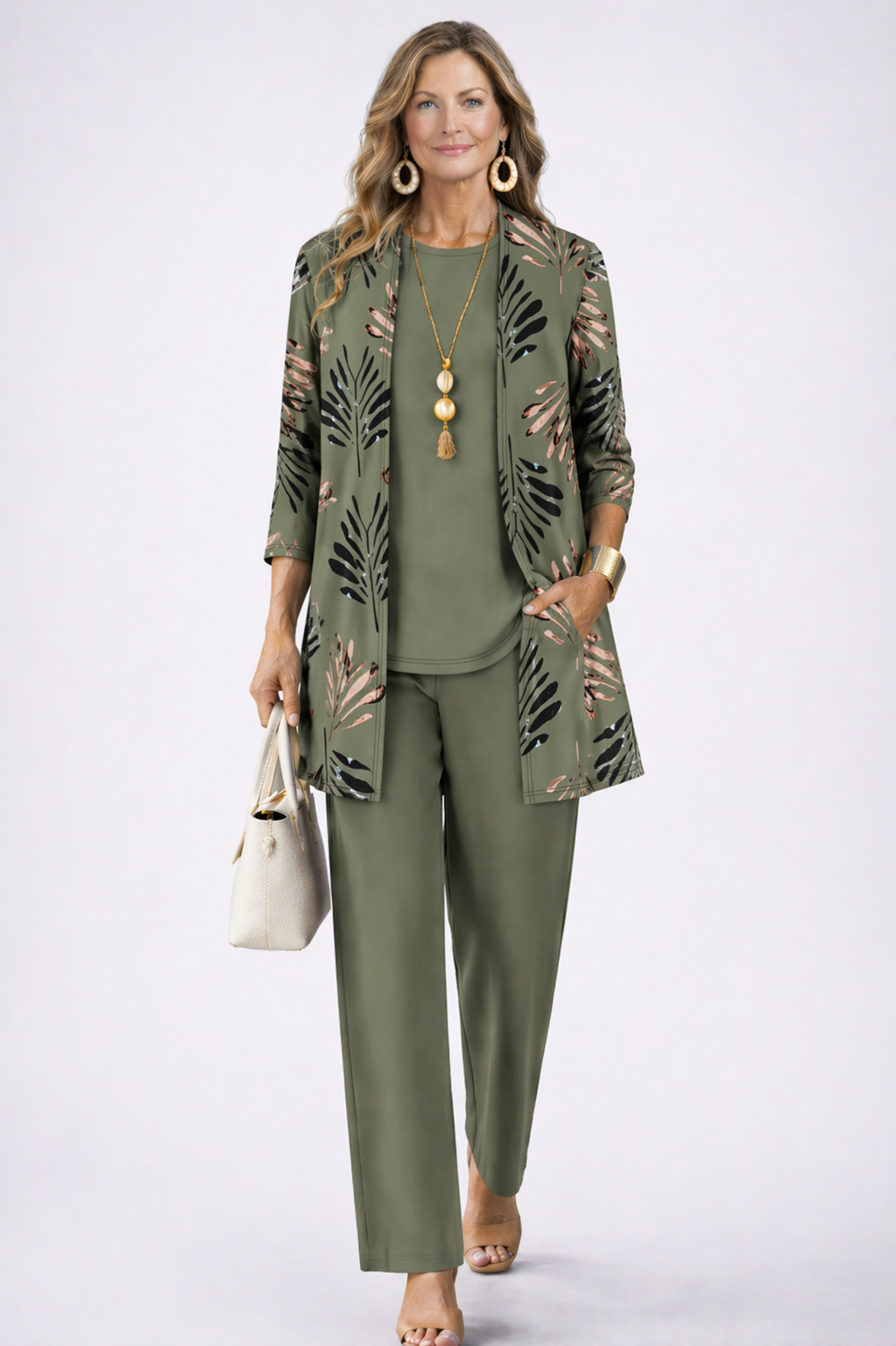 Femme en ensemble vert kaki : cardigan ouvert à feuilles noires et rosées, haut uni, pantalon droit, main dans la poche. 2