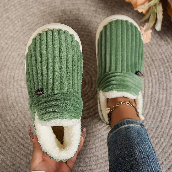 Chaussons verts côtelés vus de dessus sur un tapis gris, l'un tenu en main, l'autre porté avec un jean. 13