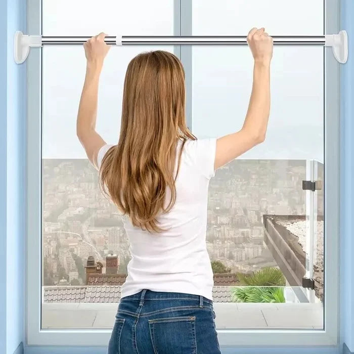 Vue de dos d'une femme qui installe la tringle en haut d'une fenêtre, en la maintenant des deux mains. 3