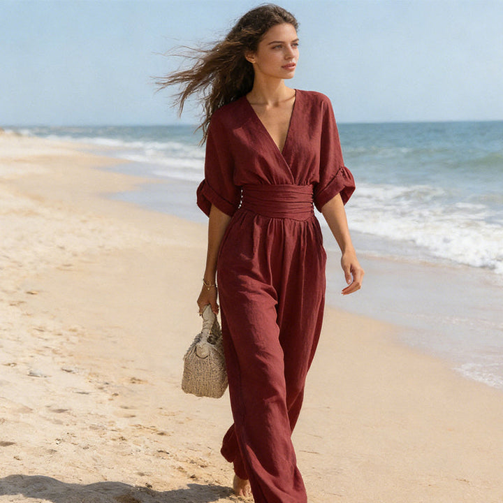 Combinaison bordeaux portée en marchant sur une plage, cheveux au vent, sac en paille à la main. 7