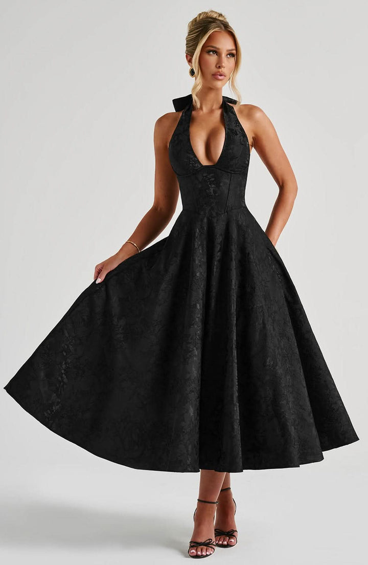 Robe noire à motif floral tonal portée de face, la mannequin tenant sa jupe ample, col licou et corsage ajusté. 13