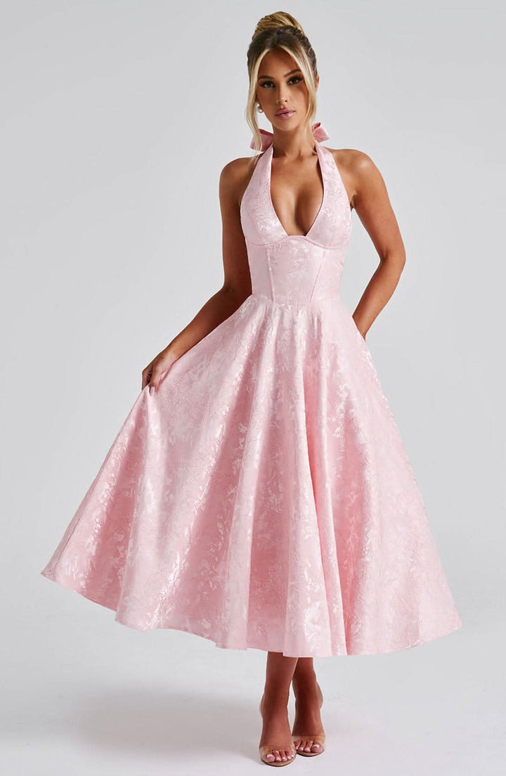 Robe rose pâle à motif floral portée de face par une mannequin qui soulève légèrement la jupe évasée. 7