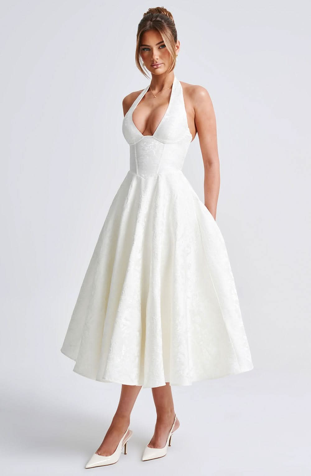 Robe ivoire vue de trois quarts sur mannequin, mettant en valeur la jupe évasée et le corsage structuré à décolleté plongeant. 2