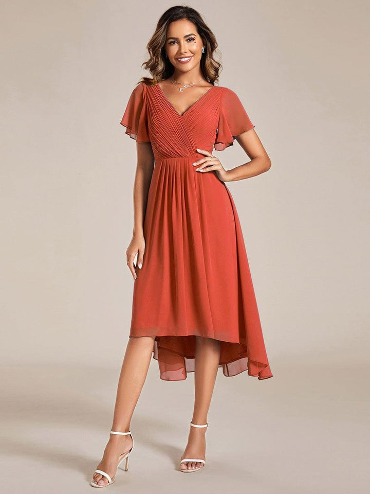 Robe orange terracotta portée de face par une mannequin, main sur la hanche, buste croisé plissé et ourlet asymétrique 92