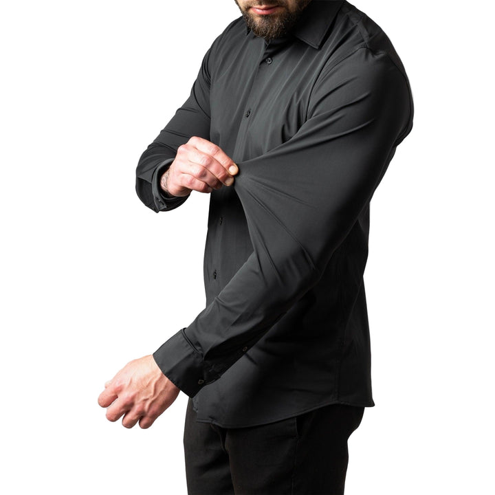 Homme en chemise noire tirant le tissu de la manche du bout des doigts pour montrer son élasticité, vue de côté. 1