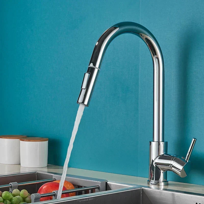 Robinet chromé à bec haut et douchette, jet d'eau coulant vers un évier avec des fruits, devant un mur bleu-vert. 1