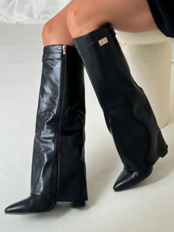 Bottes hautes noires en simili cuir brillant portées assise, zip latéral et boucle dorée sur la sangle visibles. 10