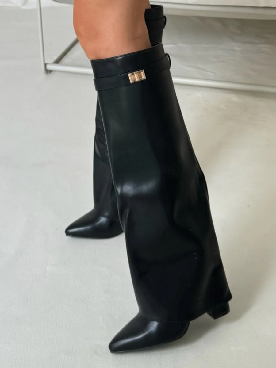 Bottes noires en simili cuir lisse portées debout, avec sangle à boucle dorée et rabat sur le pied pointu. 11