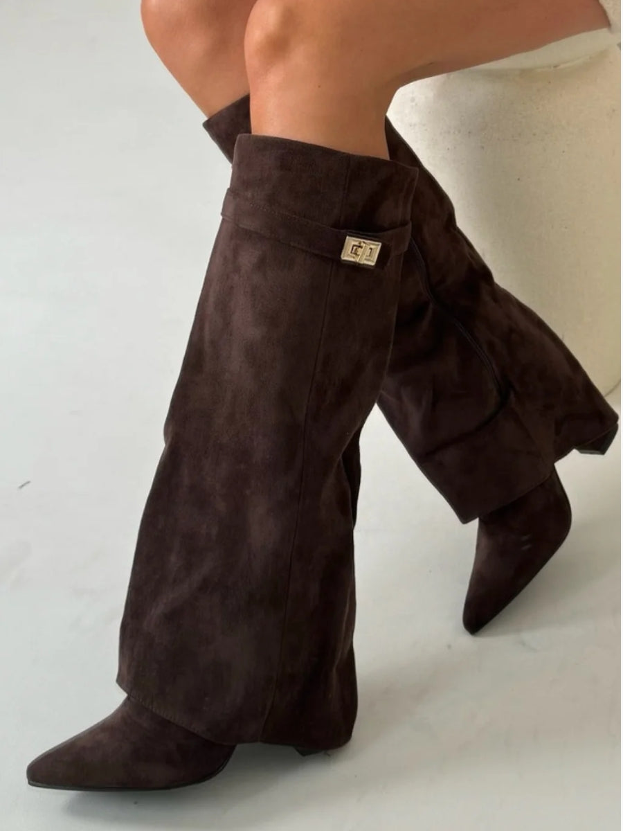 Bottes marron foncé en daim portées par un mannequin assis, avec rabat sur le pied et boucle dorée sur la sangle. 14
