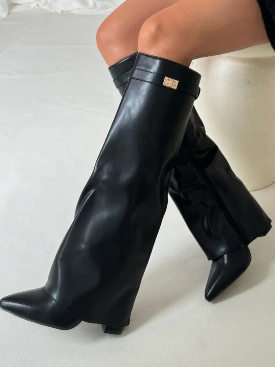 Bottes hautes noires en simili cuir portées assise sur un tabouret, boucle dorée sur la sangle et bout pointu. 15