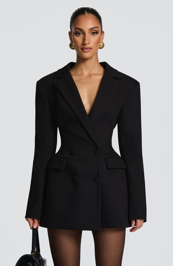 Vue de face de la robe blazer noire, double boutonnage, poches à rabat, taille marquée et large décolleté en V. 6