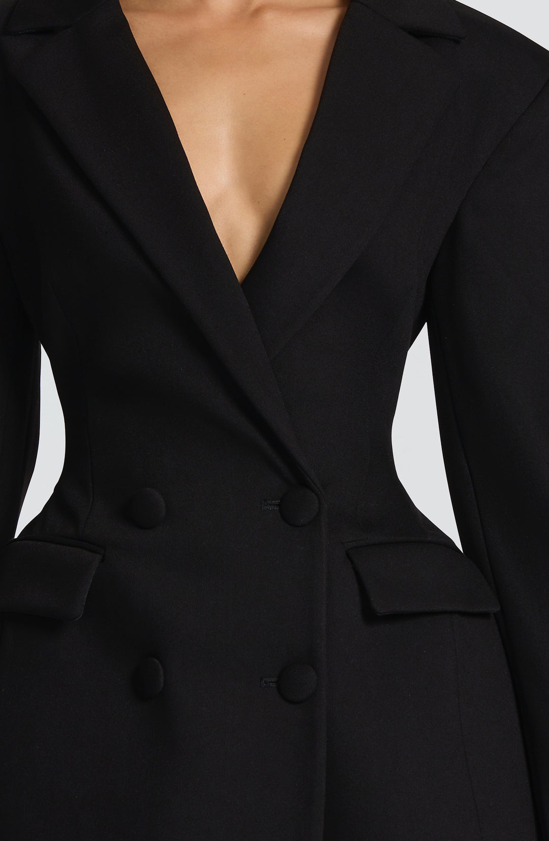 Détail du buste de la robe blazer noire: revers cranté, quatre boutons recouverts de tissu, poches à rabat et taille cintrée. 12