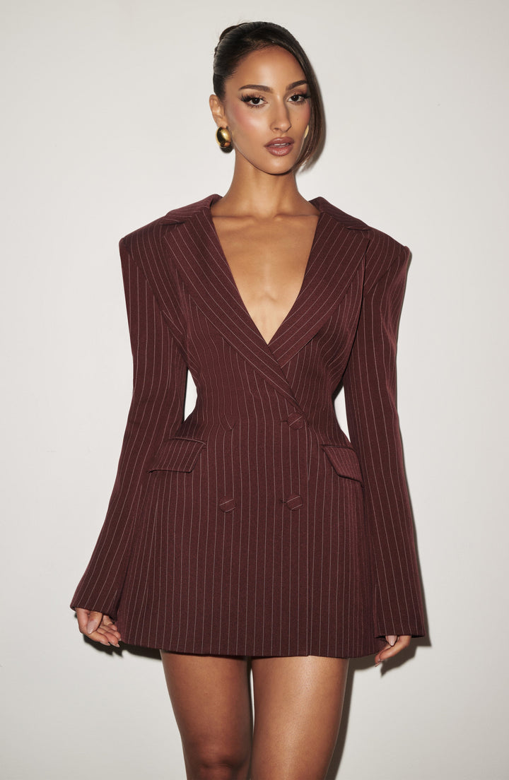 Gros plan de face sur une femme en robe blazer bordeaux à fines rayures, décolleté profond, boutons croisés et poches à rabat. 21