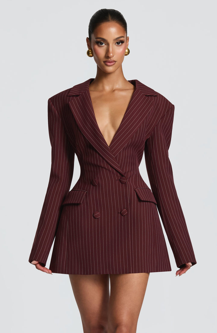 Buste et jupe de face en robe blazer bordeaux à fines rayures claires, décolleté profond et poches à rabat sur fond clair. 28