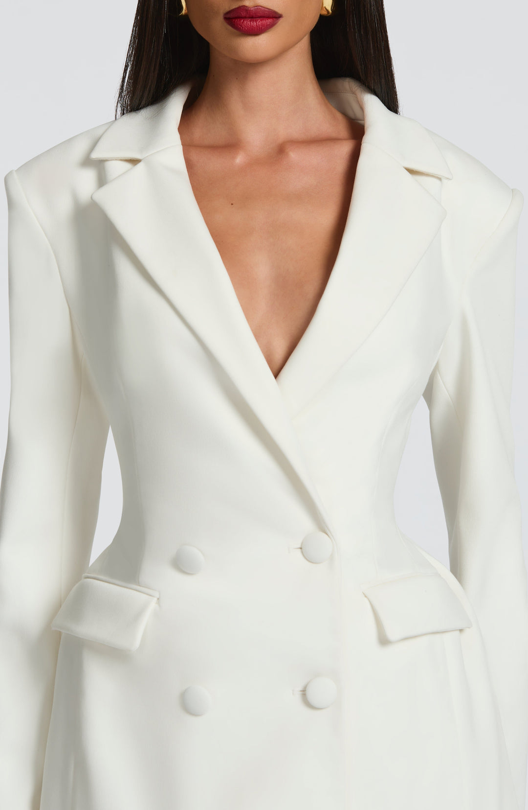 Gros plan sur le buste de la robe blazer blanche: col cranté en V profond, boutons recouverts de tissu et poches à rabat. 15