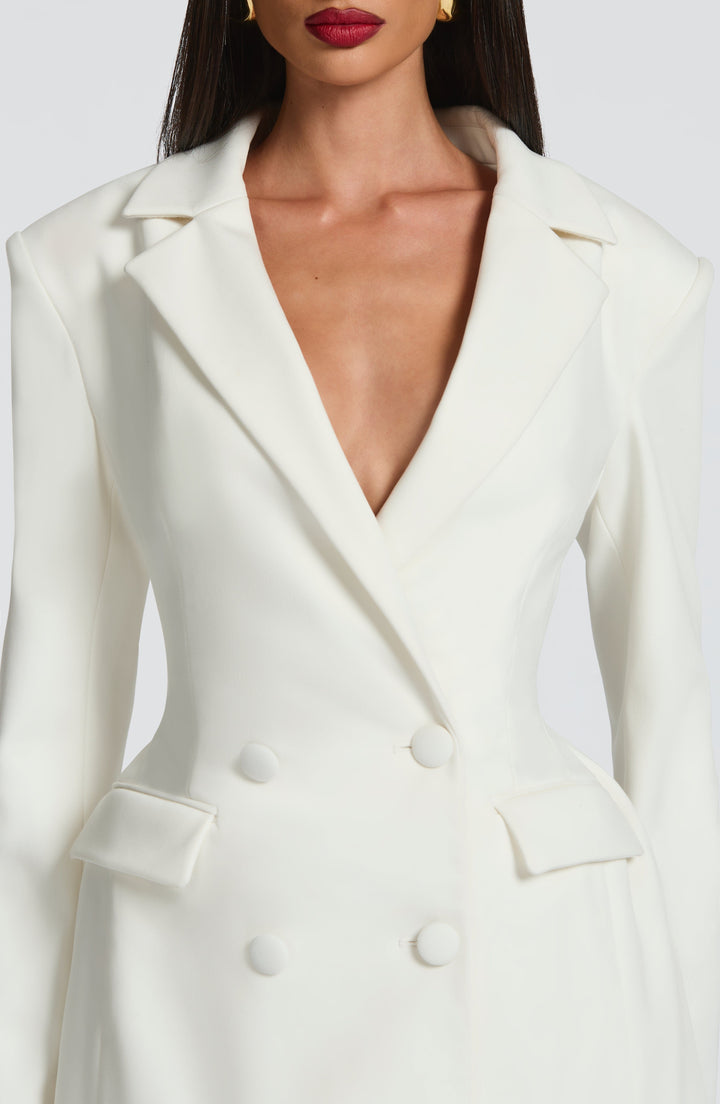 Gros plan sur le buste de la robe blazer blanche: col cranté en V profond, boutons recouverts de tissu et poches à rabat. 15