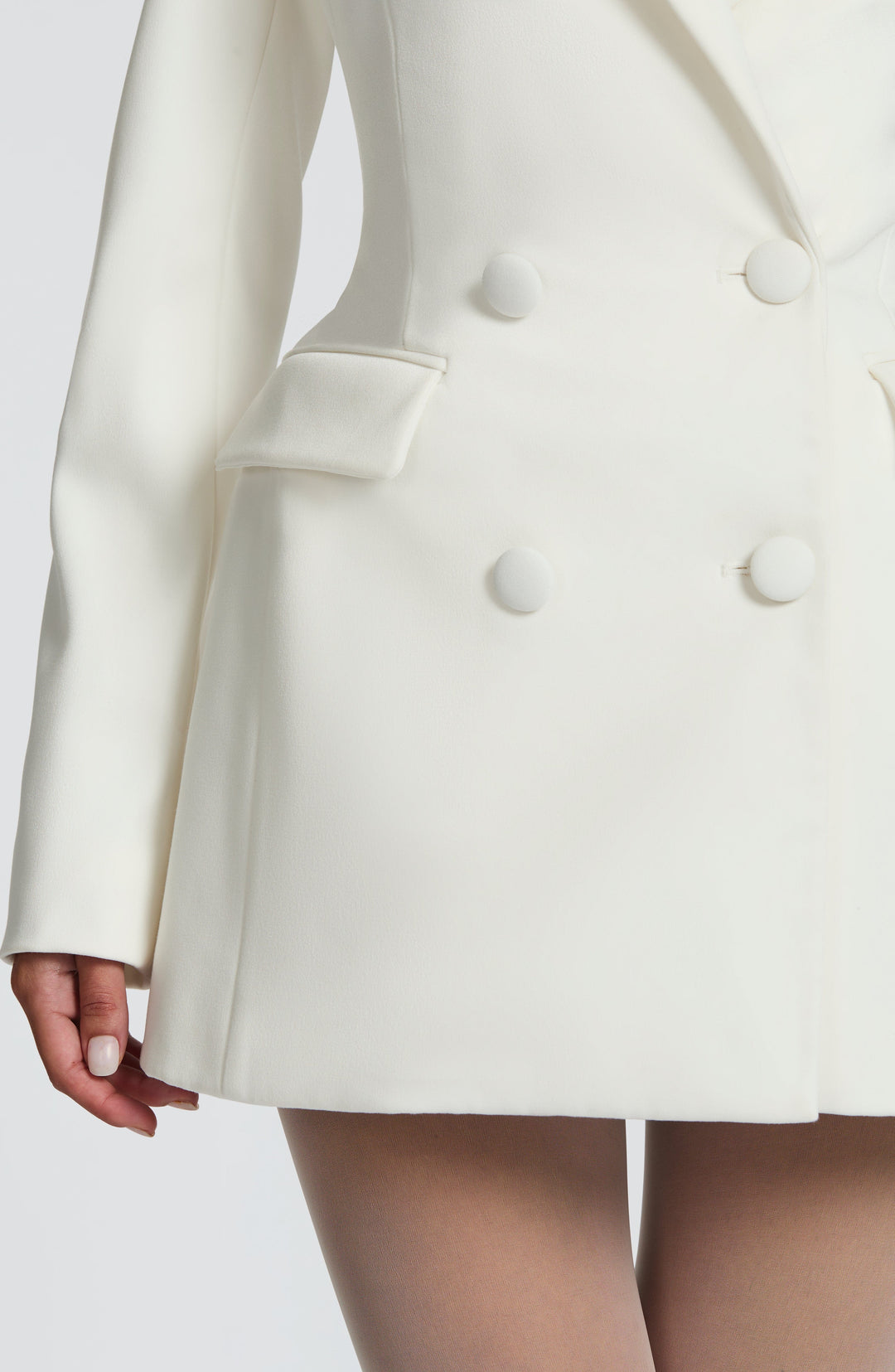 Détail du bas de la robe blazer blanche: boutons recouverts de tissu, poche à rabat, manche longue et ourlet évasé. 16