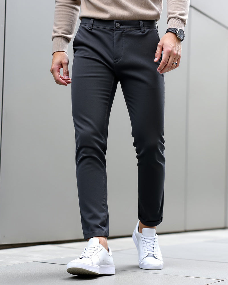 Chino anthracite porté avec un pull beige, une montre et des baskets blanches devant un mur gris. 9