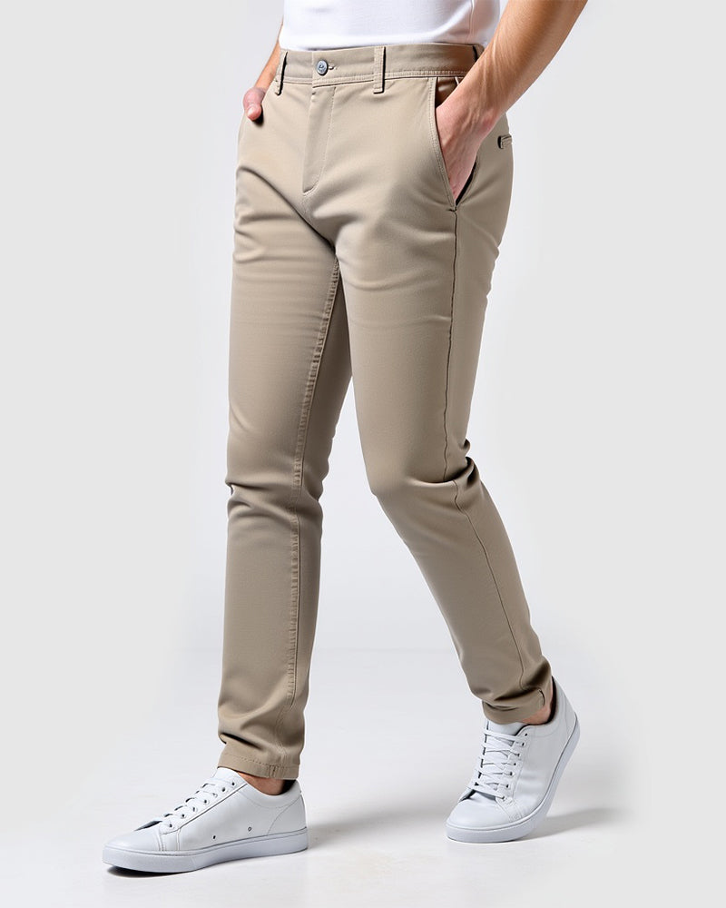 Chino beige sable porté de trois quarts avec un t-shirt blanc, les mains dans les poches et des baskets blanches. 14