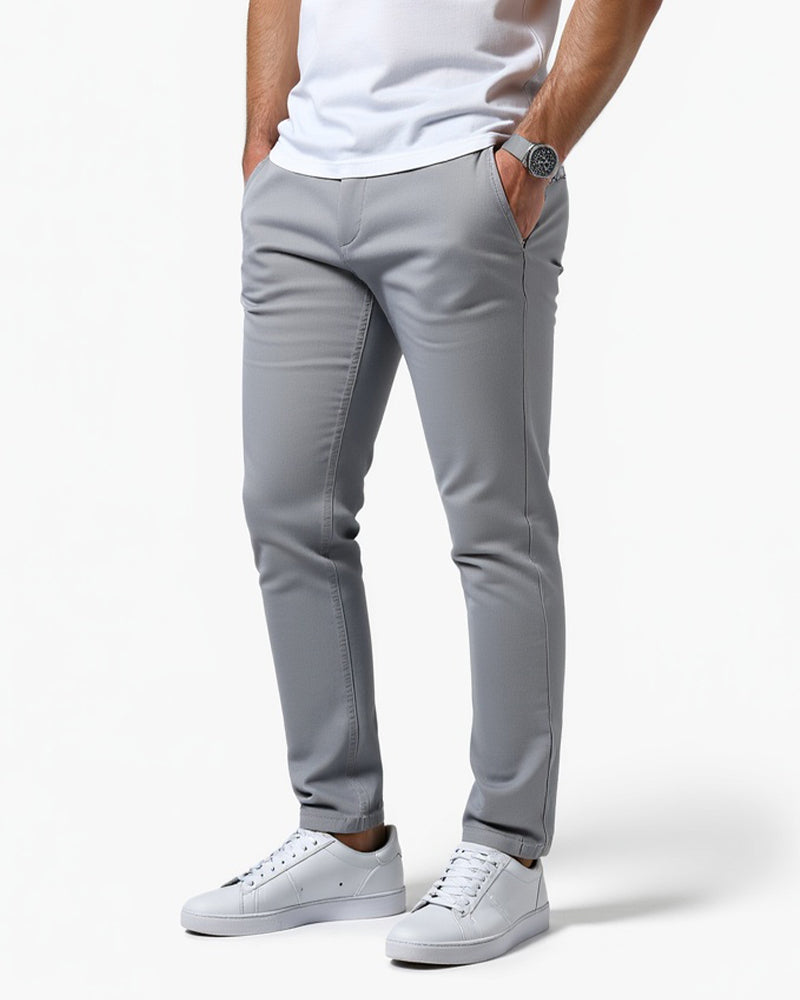 Chino gris clair porté de trois quarts avec un t-shirt blanc, une main dans la poche et des baskets blanches. 1