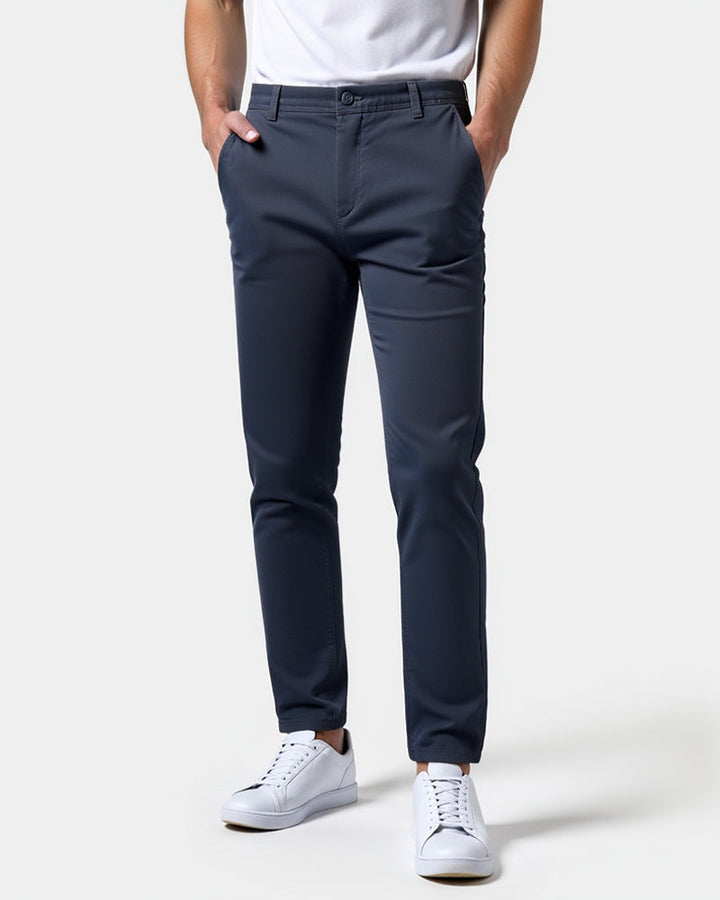 Chino bleu marine porté de face avec un t-shirt blanc, les mains dans les poches et des baskets blanches. 15