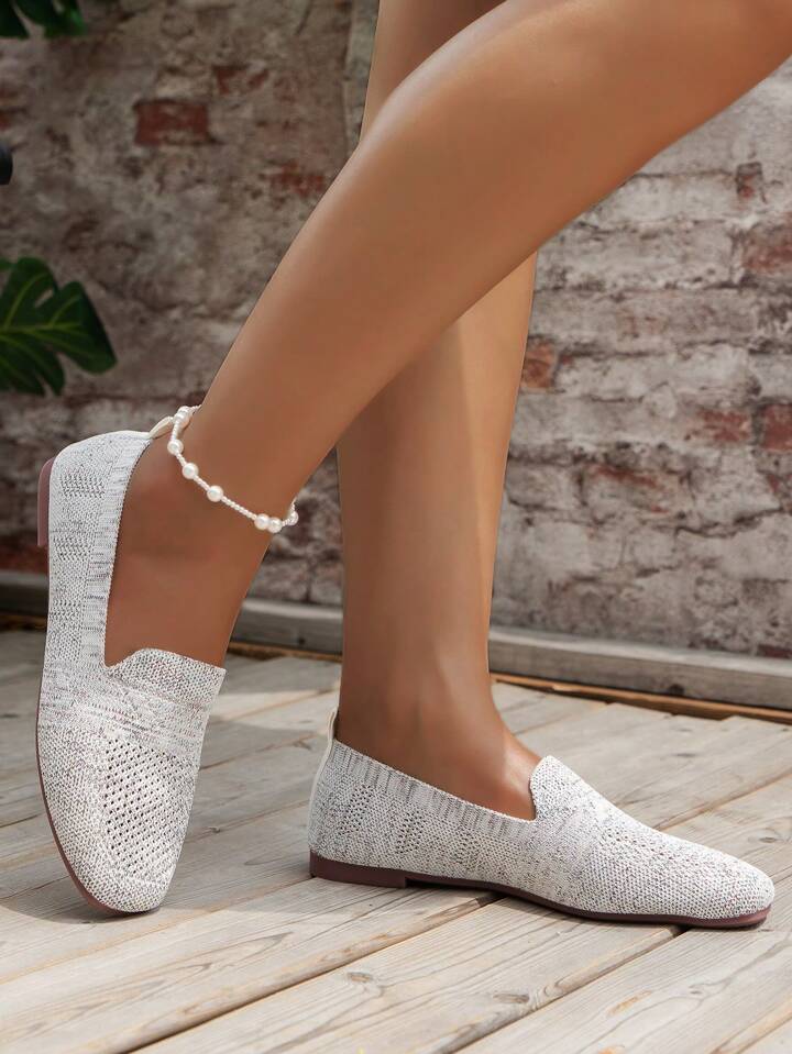 Paire grise claire en maille tricotée portée avec un bracelet de cheville en perles, devant un mur de briques. 14