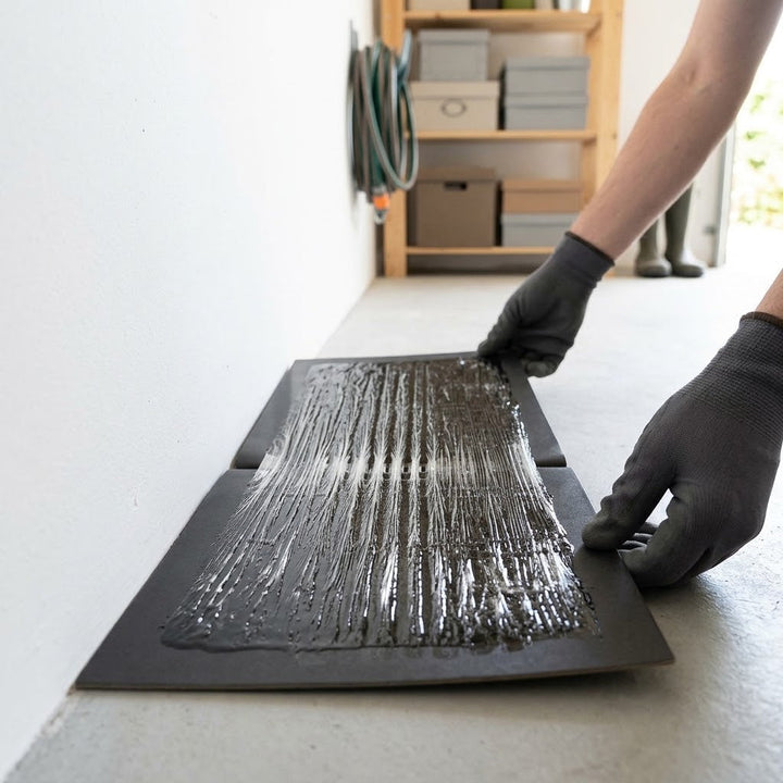 Mains gantées dépliant et posant la plaque de colle noire le long d'un mur de garage 4