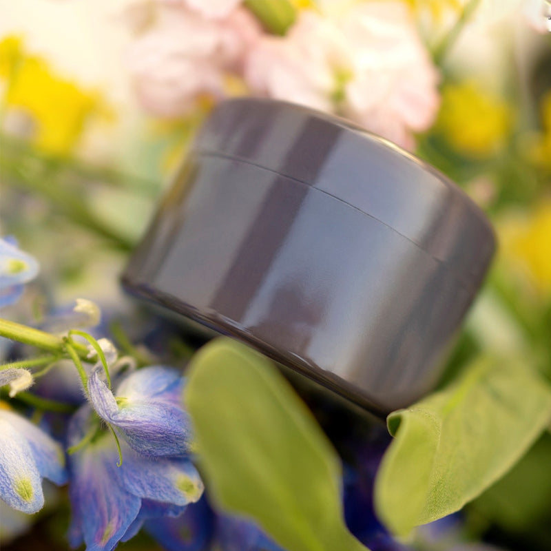 Insert gris foncé brillant posé parmi des fleurs bleues, roses et jaunes et des feuilles vertes. 10