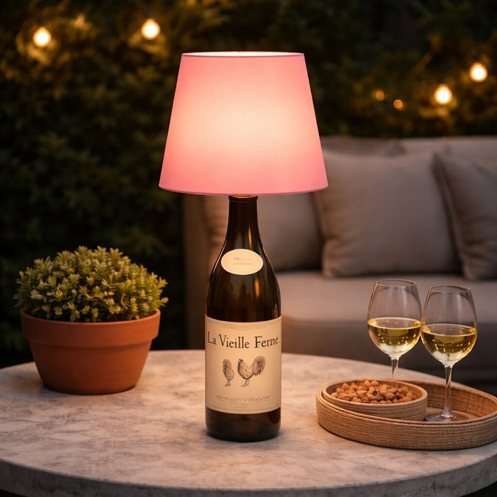 Abat-jour rose allumé sur une bouteille de vin blanc, sur une table de terrasse avec deux verres 19