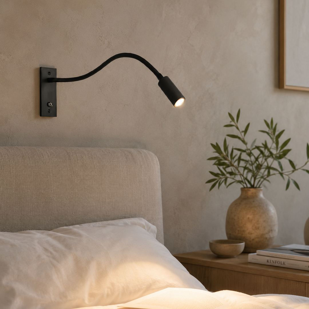 Applique noire allumée au-dessus d'un lit aux draps blancs, dans une chambre aux murs en enduit beige, avec vase et branchage. 3
