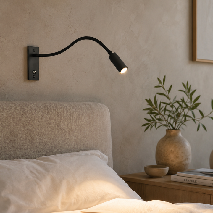 Applique noire allumée au-dessus d'un lit aux draps blancs, dans une chambre aux murs en enduit beige, avec vase et branchage. 3