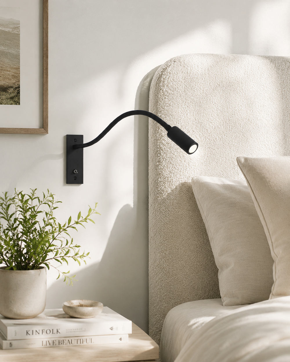 Applique noire fixée au mur à côté d'une tête de lit en tissu bouclé crème, avec plante et livres sur la table de chevet. 2