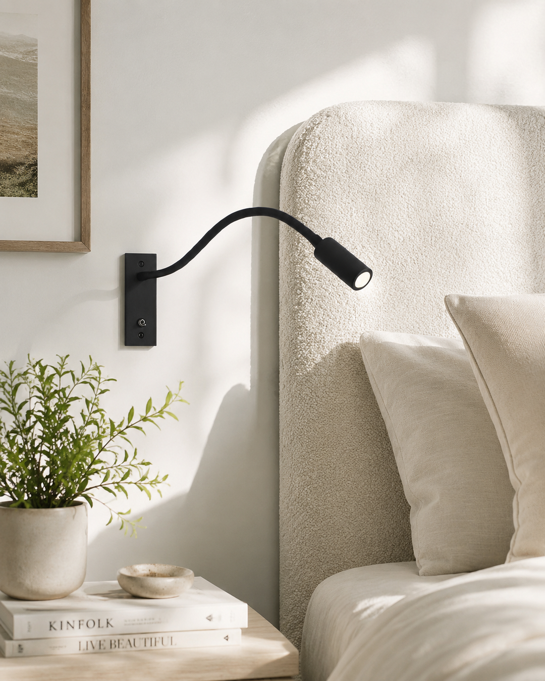Applique noire fixée au mur à côté d'une tête de lit en tissu bouclé crème, avec plante et livres sur la table de chevet. 2