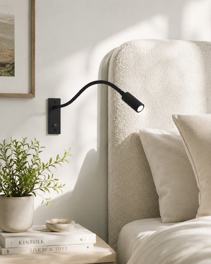 Applique noire fixée au mur à côté d'une tête de lit en tissu bouclé crème, avec plante et livres sur la table de chevet. 2