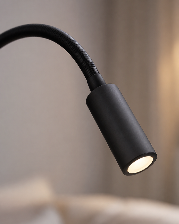 Gros plan sur la tête cylindrique noire de la lampe et son bras flexible, la LED allumée diffusant une lumière chaude. 4