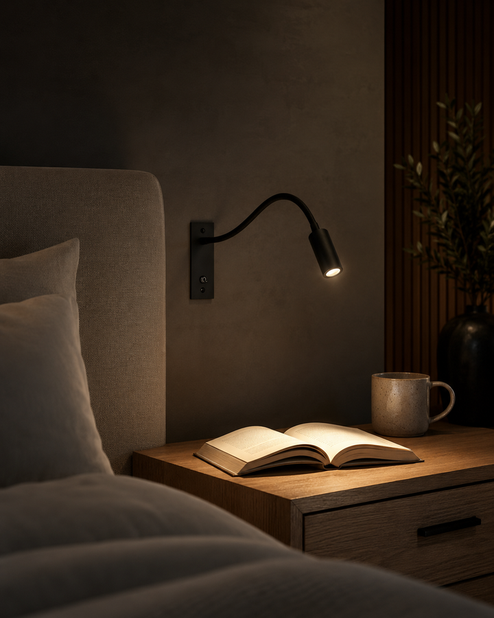 Applique noire allumée dans une chambre sombre, éclairant un livre ouvert posé sur une table de chevet en bois à côté d'une tasse. 6