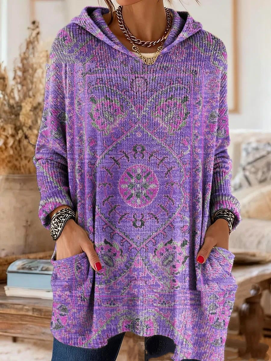 Version violette de la tunique à capuche, motif de tapis rose et vert sur maille côtelée, portée avec les mains dans les poches. 2