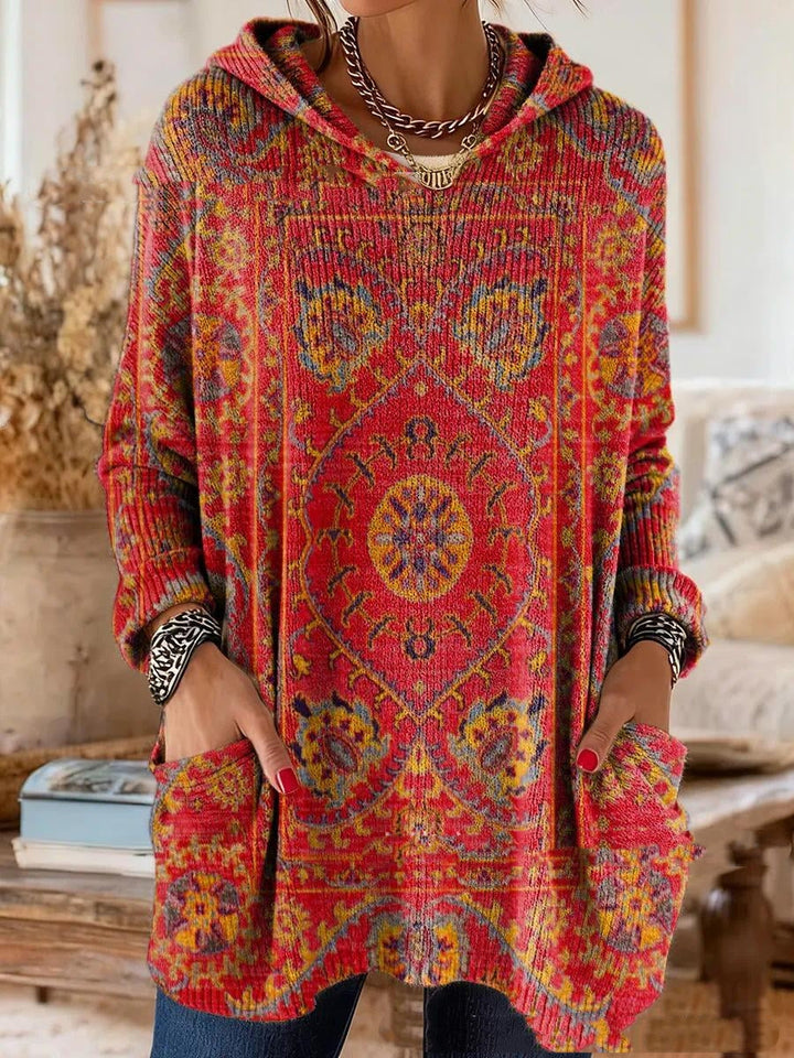 Version rouge au motif de tapis oriental jaune et bleu, vue de face portée par un mannequin, capuche et poches avant visibles. 4