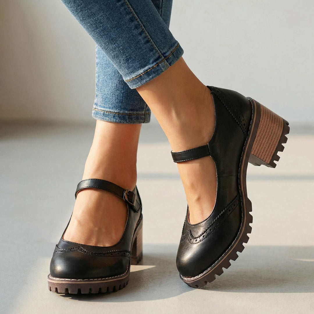 Mary Janes noires à talon bloc imitation bois portées avec un jean, vue de face sur fond clair, bride à boucle et perforations. 1
